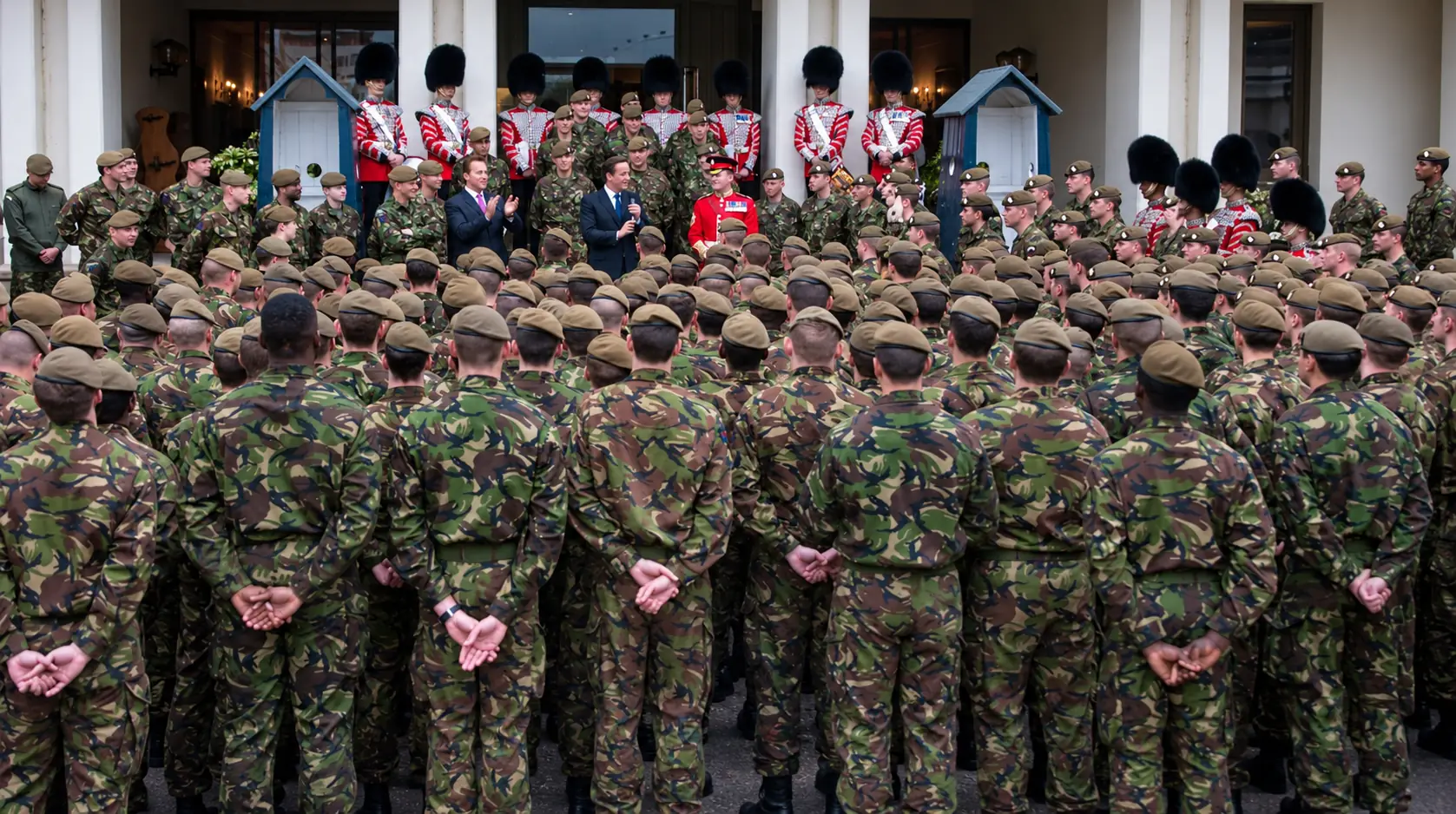 Soldiers in combat dress formed up in front of Guardsmen in red tunics and bearskins