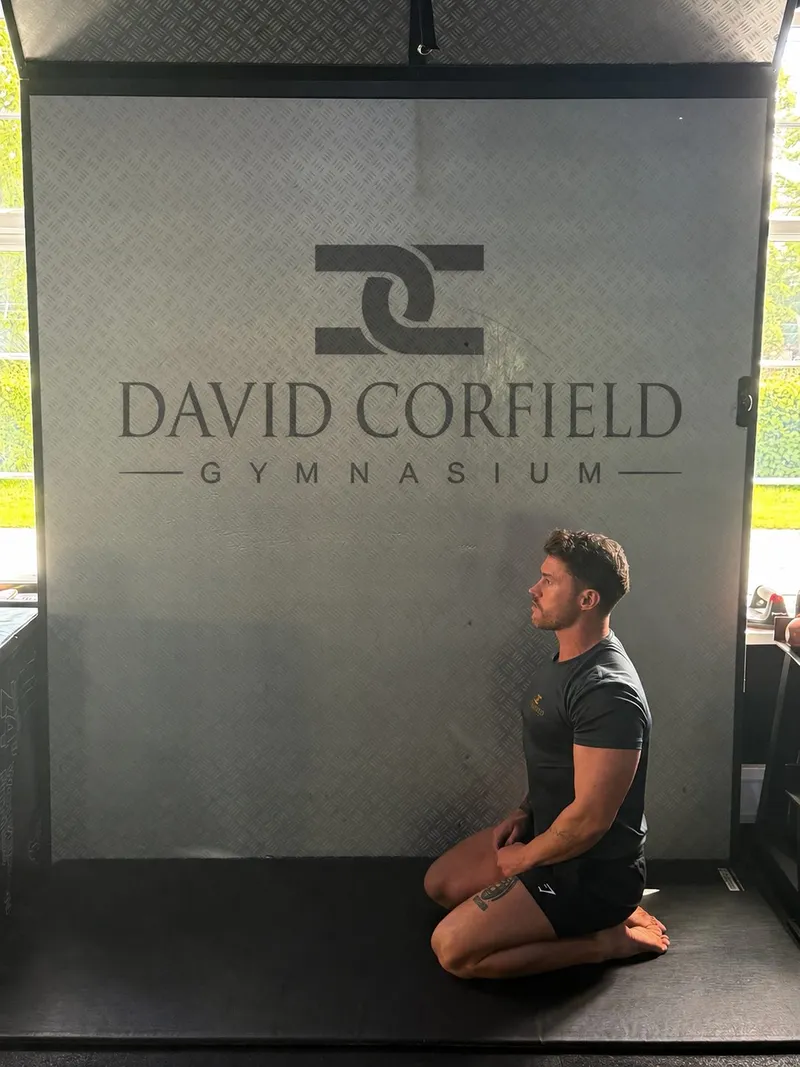Alex kneeling beneath the David Corfield Gymnasium sign